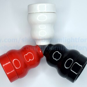May include: Three ceramic bottle stoppers in a triangular arrangement. The stoppers are white, red, and black. Each stopper has a unique design with two circles on the front.