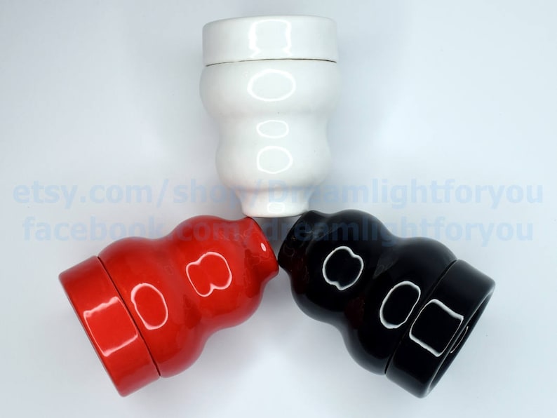 May include: Three ceramic bottle stoppers in a triangular arrangement. The stoppers are white, red, and black. Each stopper has a unique design with two circles on the front.