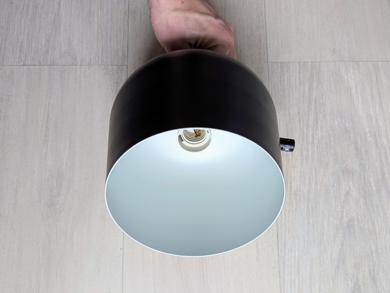 May include: A black and white pendant light fixture with a white interior and a black exterior. The light is turned on and the bulb is visible.