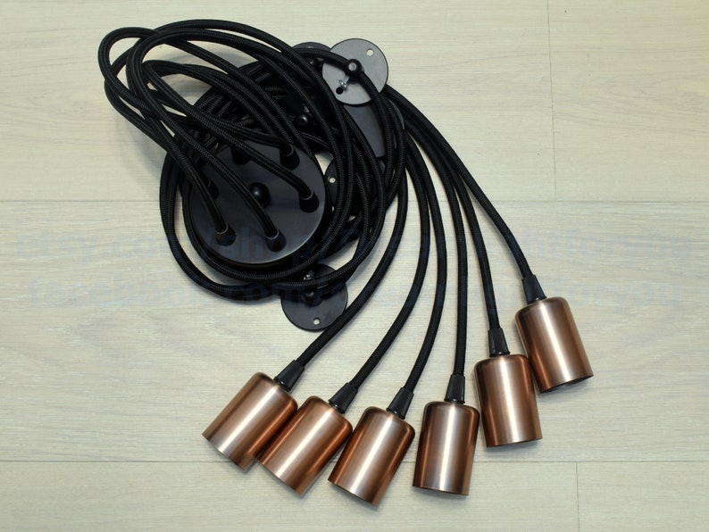 May include: A black ceiling light fixture with six copper-colored lampshades hanging from black cords.
