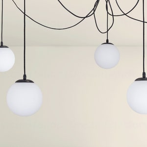 May include: Five white globe pendant lights hang from black cords against a white wall. The lights are all the same size and shape.