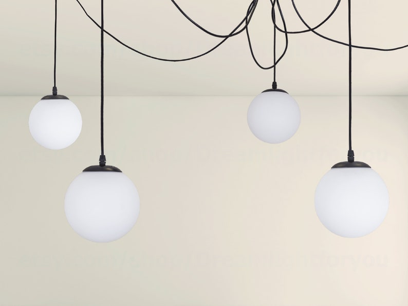 May include: Five white globe pendant lights hang from black cords against a white wall. The lights are all the same size and shape.
