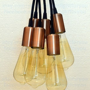 May include: A cluster of six copper pendant lights with clear glass bulbs hanging from black cords.