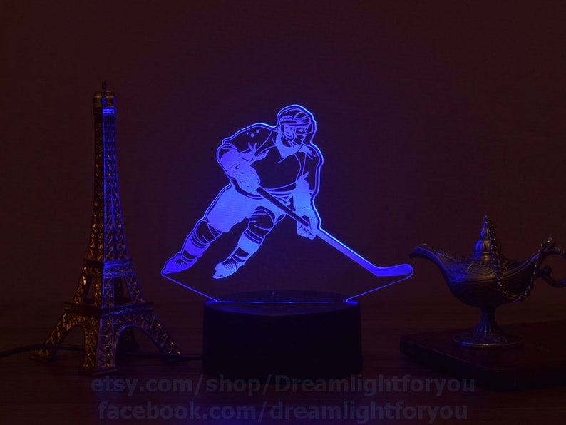 May include: A blue LED night light with a silhouette of a hockey player skating with a stick. The light is on a black base and is illuminated with a blue glow.