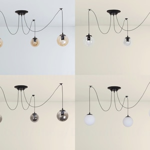 May include: Four black pendant lights with clear and amber glass shades hanging from a ceiling. The lights are connected by black cords and have a unique, modern design.