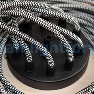 May include: Close-up of a black ceiling light fixture with six black and white braided cords. The cords are twisted together and have a zig-zag pattern.