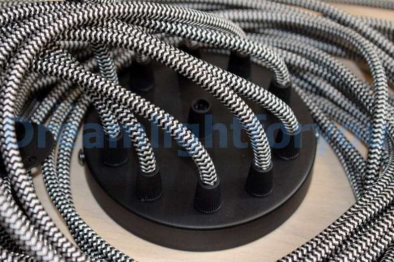 May include: Close-up of a black ceiling light fixture with six black and white braided cords. The cords are twisted together and have a zig-zag pattern.