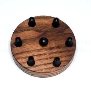 K&ouml;nnte beinhalten: Eine runde Holz-Deckenrosette mit sechs schwarzen elektrischen Kabelanschl&uuml;ssen. Die Rosette ist aus dunkel gebeiztem Holz mit nat&uuml;rlicher Holzmaserung.