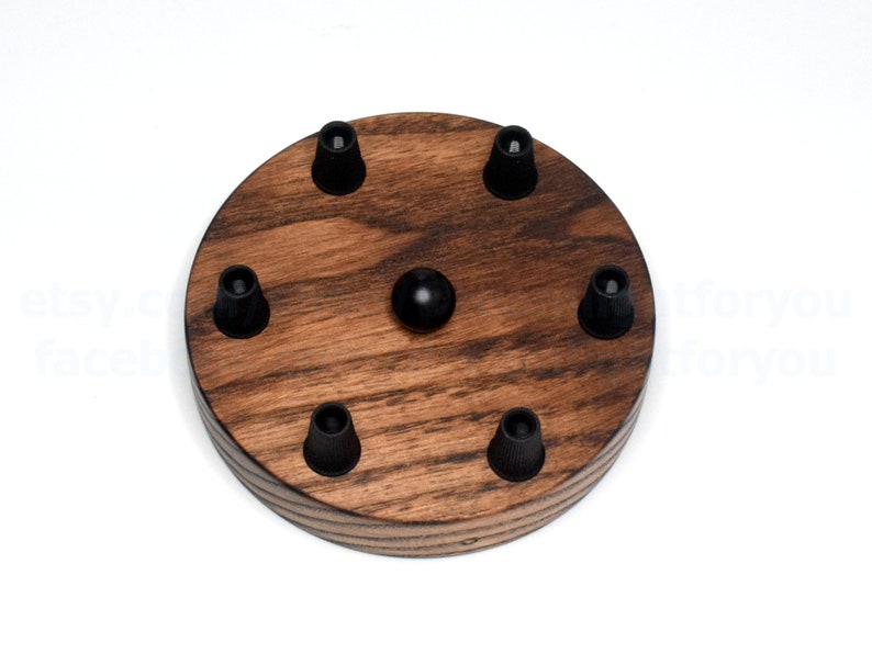 K&ouml;nnte beinhalten: Eine runde Holz-Deckenrosette mit sechs schwarzen elektrischen Kabelanschl&uuml;ssen. Die Rosette ist aus dunkel gebeiztem Holz mit nat&uuml;rlicher Holzmaserung.