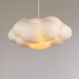 May include: A cloud-shaped pendant light fixture. The light is a soft white color, with a textured surface. The light hangs from a white cord and emits a warm glow from within.
