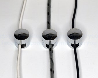 Puede incluir: Tres clips de cable cromados con diferentes cables de colores que pasan a través de ellos. Los cables son blanco, gris con rayas negras y negro.