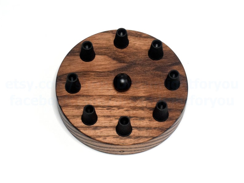 K&ouml;nnte beinhalten: Eine runde Holz-Deckenrosette mit acht schwarzen Kabelhaltern. Die Rosette ist aus dunkel gebeiztem Holz mit nat&uuml;rlicher Holzmaserung.