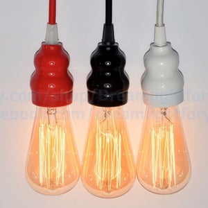 May include: Three hanging light bulbs with different colored ceramic lampshades. The shades are red, black, and white. The bulbs are turned on and glowing.