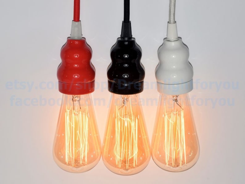 May include: Three hanging light bulbs with different colored ceramic lampshades. The shades are red, black, and white. The bulbs are turned on and glowing.