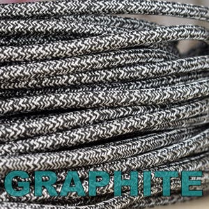 May include: Close-up of a spool of black and white braided electrical cord. The cord has a textured, herringbone pattern. The word "GRAPHITE" is printed in teal on the cord.