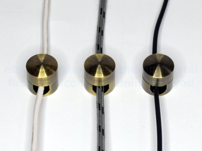 May include: Three antique brass cable clips with different colored cords running through them. The cords are white, gray, and black.