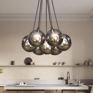 May include: A contemporary chandelier featuring seven smoked glass globe shades. Each globe hangs from a dark cord, reflecting light. The fixture is suspended above a kitchen island, providing a modern lighting solution.