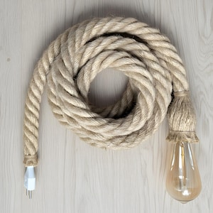 Könnte beinhalten: Eine gewickelte, dicke Seilleuchte mit einer Edison-Glühbirne im Vintage-Stil. Das beige Seil bildet eine kreisförmige Form, mit einem weißen Stecker an einem Ende. Die Glühbirne hängt am Ende des Seils.