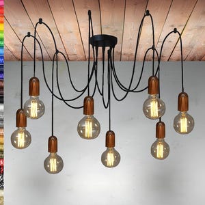 Puede incluir: Una lámpara de araña de metal negro con ocho bombillas. Las bombillas están suspendidas del techo por cables negros y tienen bases de madera. Las bombillas están encendidas y emiten un brillo cálido.