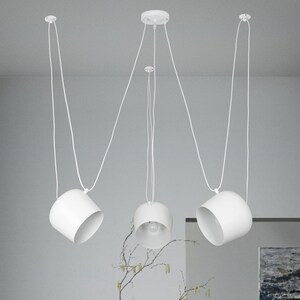 May include: Three white pendant lights with round shades hanging from the ceiling. The lights are suspended by white cords.