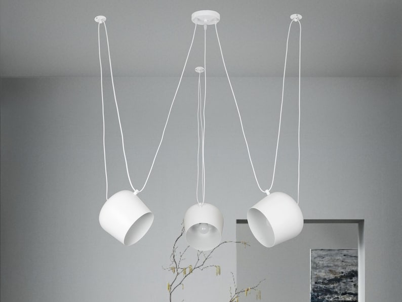 May include: Three white pendant lights with round shades hanging from the ceiling. The lights are suspended by white cords.
