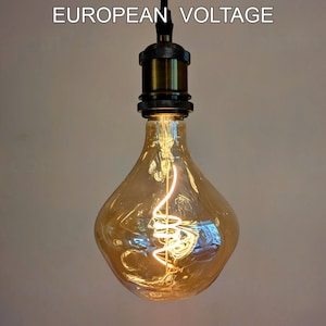 Könnte beinhalten: Eine klare Glühbirne aus Glas mit einem spiralförmigen Filament im Inneren. Die Birne hat die Form einer Träne und einen messingfarbenen Sockel. Die Birne ist eingeschaltet und leuchtet.