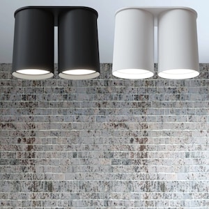 May include: Two black and two white cylindrical ceiling lights mounted on a brick wall.