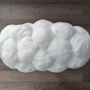 May include: A white, cloud-shaped decorative object with a textured, crinkled surface. The form consists of multiple rounded, bulbous sections that mimic the appearance of a cumulus cloud, featuring a matte finish and a soft, organic silhouette.