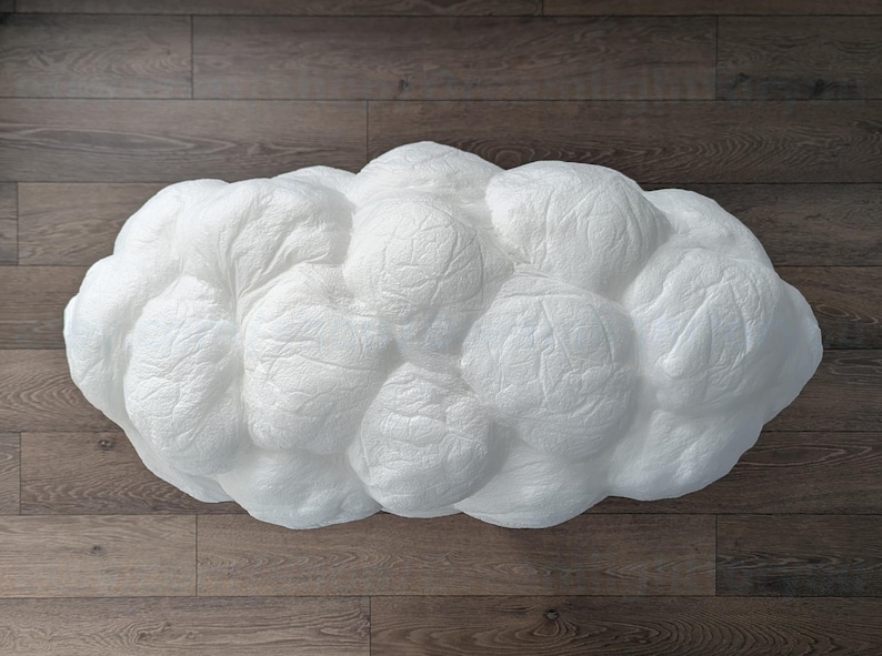 May include: A white, cloud-shaped decorative object with a textured, crinkled surface. The form consists of multiple rounded, bulbous sections that mimic the appearance of a cumulus cloud, featuring a matte finish and a soft, organic silhouette.