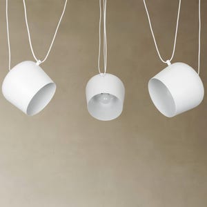 May include: Three white pendant lights hanging from the ceiling. The lights are round and have a simple, modern design.