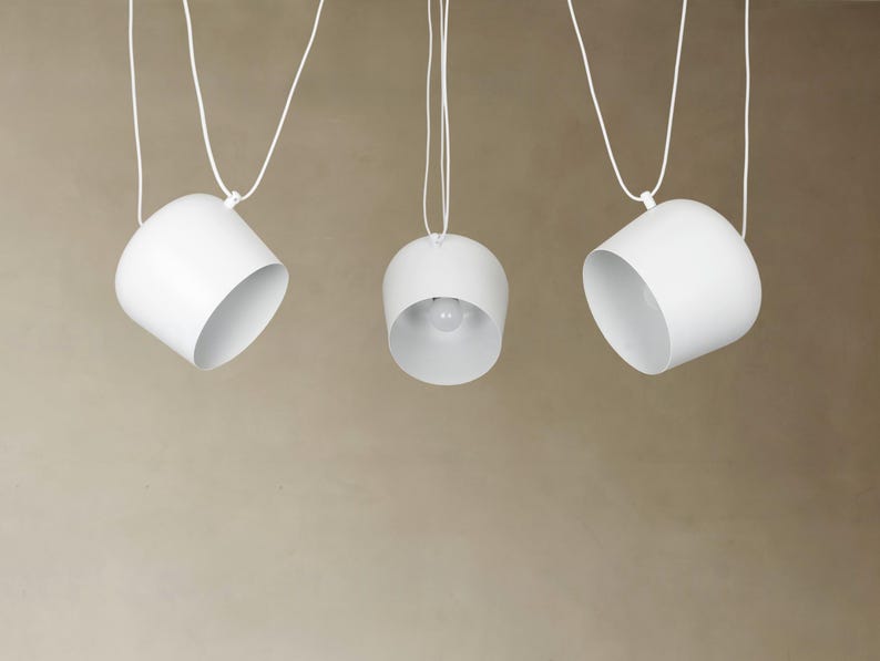 May include: Three white pendant lights hanging from the ceiling. The lights are round and have a simple, modern design.