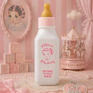 May include: A white bottle with a yellow nipple and a pink cap. The bottle features a pink graphic of a person's face and the text "Melanie Martinez", "CRY BABY", "PERFUME MILK", and "NOT FOR CONSUMPTION" with three small pink hearts below.