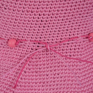 Pink crocheted sun hat with a pink ribbon tied in a bow at the crown. The ribbon has pink beads at the ends.