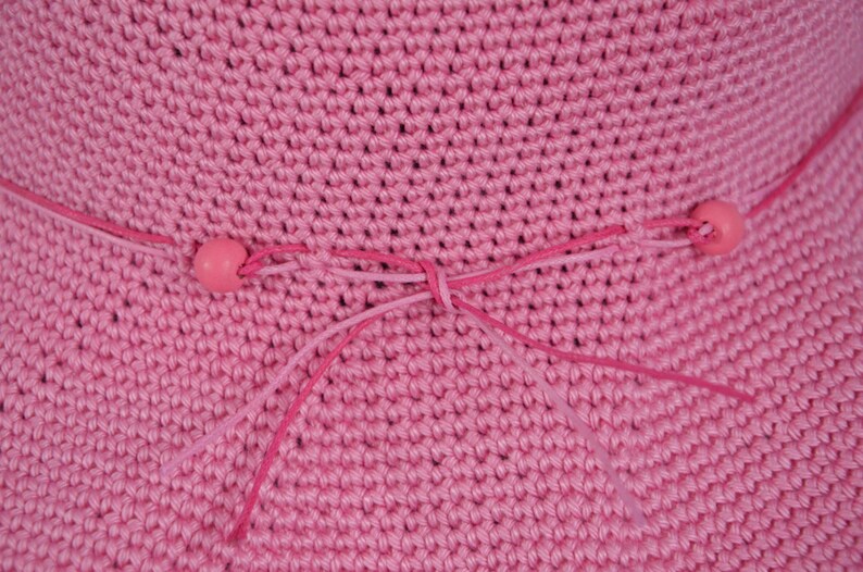Pink crocheted sun hat with a pink ribbon tied in a bow at the crown. The ribbon has pink beads at the ends.