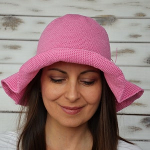 A pink crocheted sun hat with a wide brim. The hat is worn by a person with brown hair.