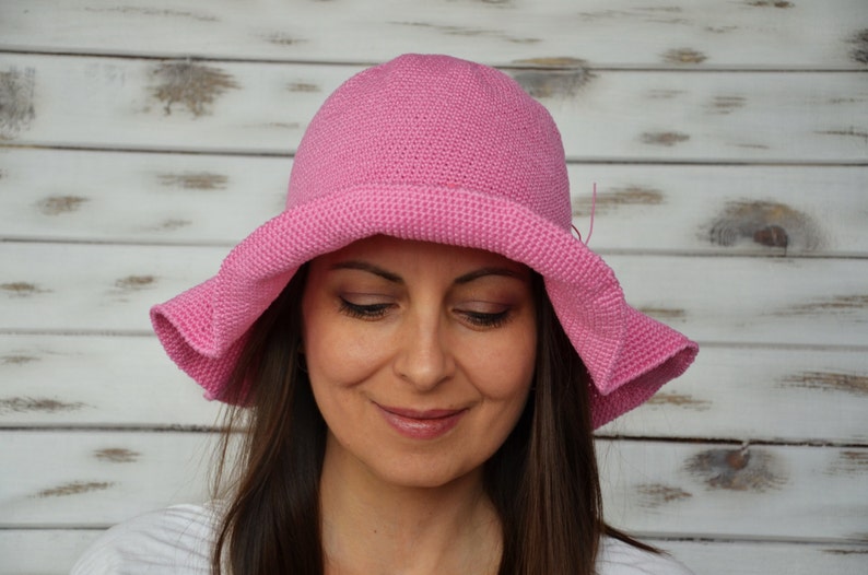 A pink crocheted sun hat with a wide brim. The hat is worn by a person with brown hair.