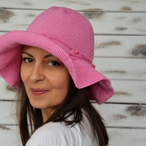 A pink crocheted sun hat with a wide brim and beaded embellishments.
