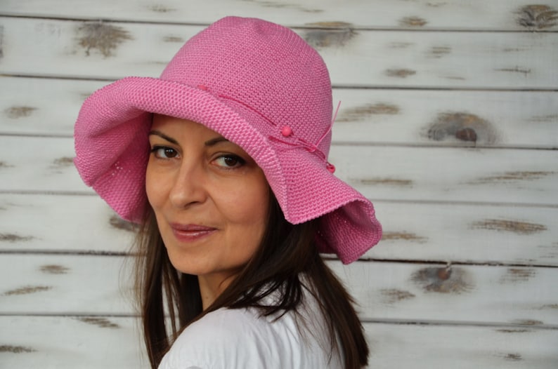 A pink crocheted sun hat with a wide brim and beaded embellishments.