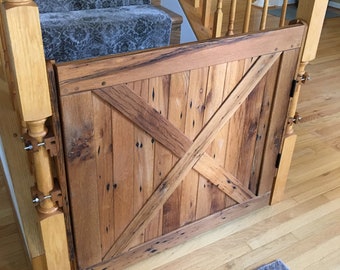 May include: A rustic wooden gate with a diagonal cross design, made from reclaimed wood planks. The gate is closed and is mounted to a wooden post. The gate is in front of a staircase with a patterned carpet.