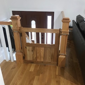 May include: A wooden gate with a white picket fence design, installed at the top of a staircase. The gate is made of natural wood with a rustic finish and has a simple latch.