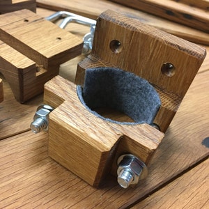 May include: Wooden wall mount with a gray felt lining for holding a rod or pipe. The mount has two screws and a metal bracket.