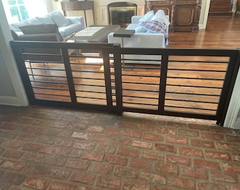 May include: A black metal gate with horizontal bars, installed in a doorway with a brick floor. The gate is closed and appears to be a safety gate for children or pets.