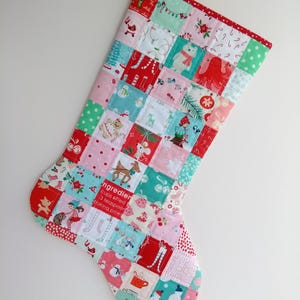 May include: A patchwork Christmas stocking constructed from various fabric squares featuring holiday-themed prints including snowmen, gingerbread, polar bears, and text reading ingredients. The stocking has a red and white polka dot hanging loop.