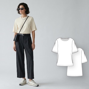 May include: A woman wearing a cream-colored short-sleeved t-shirt, dark gray pleated trousers, and white sneakers. She is also wearing sunglasses and a black crossbody bag. A line drawing of a white t-shirt is in the background.