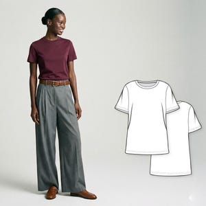 Può includere: Una donna indossa una maglietta bordeaux, pantaloni grigi a gamba larga e cintura e mocassini in pelle marrone. Due contorni di magliette bianche a destra. L'outfit è semplice e classico.