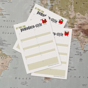 May include: Three white Pomodoro-style planning sheets with the text "GET THINGS DONE" and "pomodoro-style" in black. Each sheet features a cartoon tomato character. The sheets are on a world map background.
