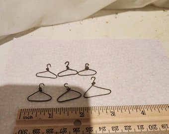 Könnte beinhalten: Sechs Miniatur-Kleiderbügel aus Draht, etwa 2,5 cm lang, sind auf einer weißen Oberfläche mit einem Lineal zur Skalierung angeordnet.