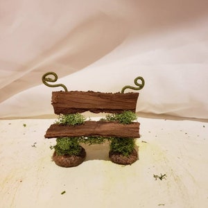 Könnte beinhalten: Eine Miniatur-Holzbänke mit Moos-Akzenten und Eichelbeinen. Die Bank hat zwei grüne Ranken, die sich an beiden Seiten nach oben winden.