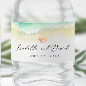 May include: A clear plastic water bottle with a white label. The label features a watercolor illustration of ocean waves and a seashell. The text on the label reads "Isabella and David June 17, 2024".