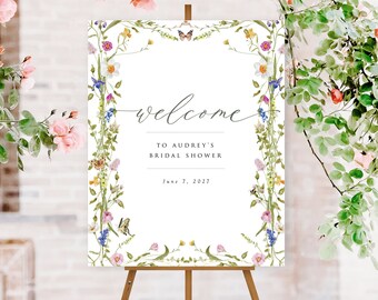 May include: A white welcome sign with a floral border and butterflies. The sign reads "Welcome to Audrey's Bridal Shower June 7, 2027".